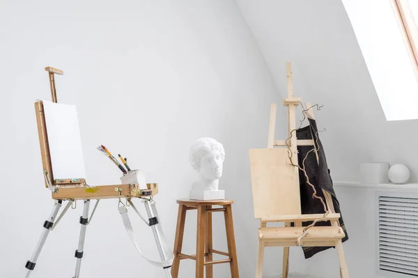 Estudio blanco y luminoso con ventana. Espacio de trabajo del artista. Caballete, lienzos y figuras de yeso para aprender a dibujar . — Foto de Stock