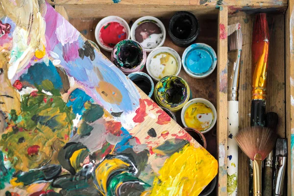Pitture di diversi colori e pennelli sporchi sul cavalletto dell'artista primo piano . — Foto Stock