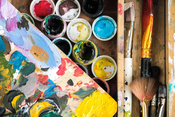 Pitture di diversi colori e pennelli sporchi sul cavalletto dell'artista primo piano . — Foto Stock