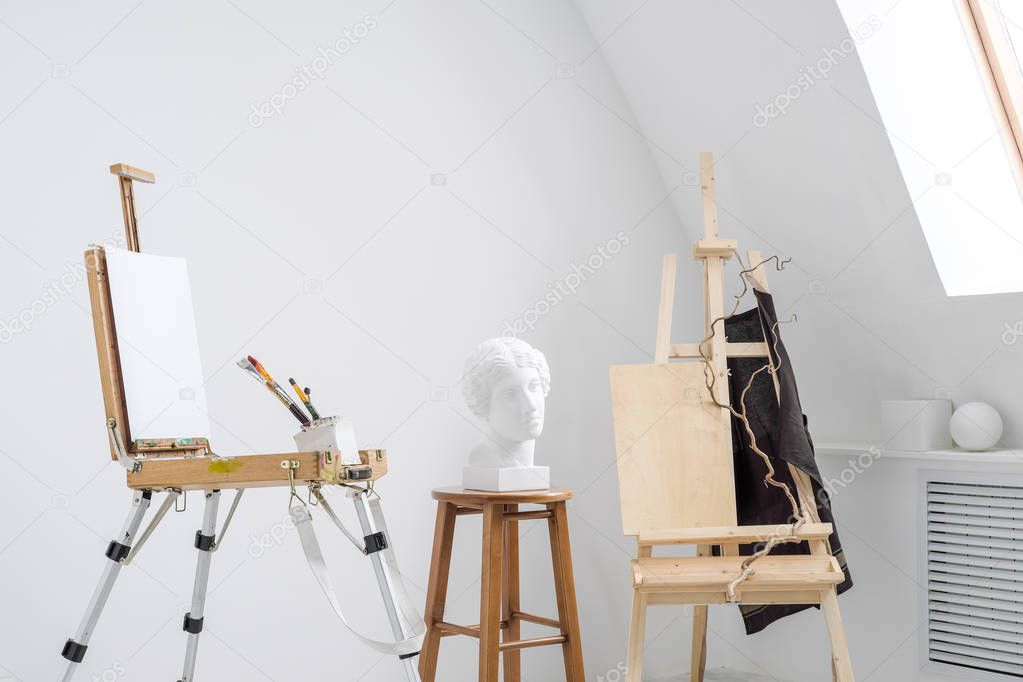 White and bright studio with a window. Workspace of the artist. Easel, canvases and plaster figures for learning to draw.
