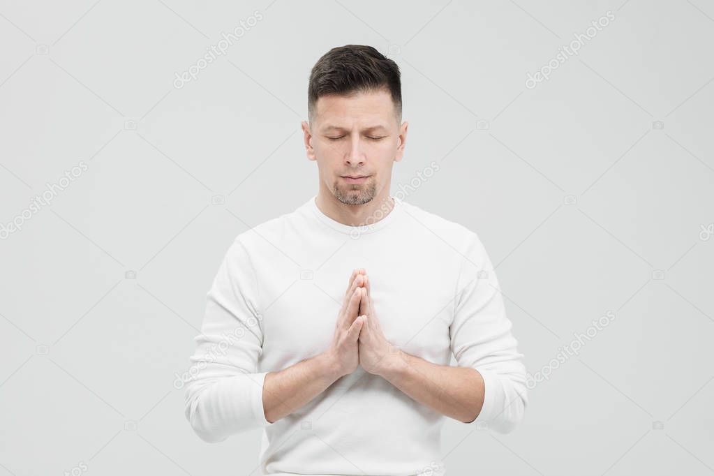 A man in white clothes on a white background with his hands folded on his chest. Meditation and prayer, yoga.