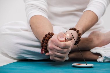 Yoga ve meditasyon kavramı. El ve ayaklarda hafif bir arka plan üzerinde Beyaz giysili bir adam close-up. Bir adam yangın bir Hint aromatik mum için ayarlar..