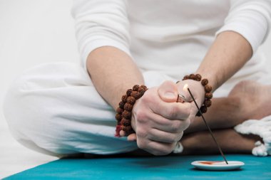 Yoga ve meditasyon kavramı. El ve ayaklarda hafif bir arka plan üzerinde Beyaz giysili bir adam close-up. Bir adam yangın bir Hint aromatik mum için ayarlar..