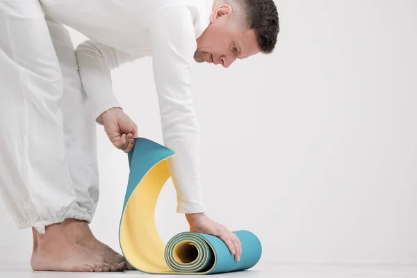 Um professor e treinador do sexo masculino em roupas brancas estão colocando um tapete de ioga amarelo e azul, preparando-se para uma aula de fitness . — Fotografia de Stock