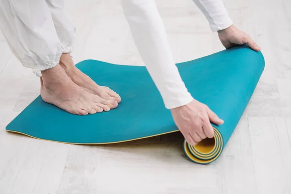 Un maestro y entrenador en ropa blanca están preparando una esterilla de yoga amarilla y azul, preparándose para una clase de fitness. . — Foto de Stock