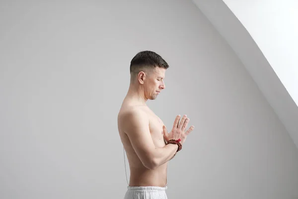 Muž v bílých šatech a rozhalenou na bílém pozadí s rukama složenýma na prsou. Meditace a modlitby, jóga. — Stock fotografie