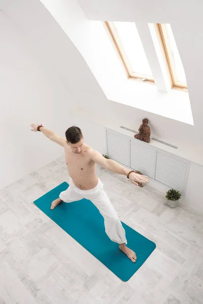 Un hombre con pantalones blancos y el pecho desnudo haciendo ejercicios. Yoga asanas y poses para estiramiento y meditación. Contra el telón de fondo de una brillante clase deportiva . — Foto de Stock