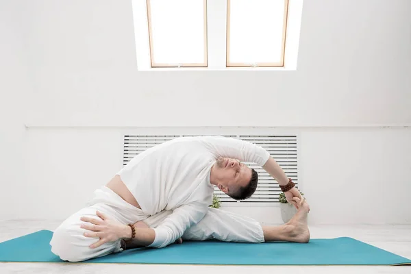 Un uomo vestito di bianco fa esercizi. Yoga asana e pose per lo stretching e la meditazione . — Foto Stock