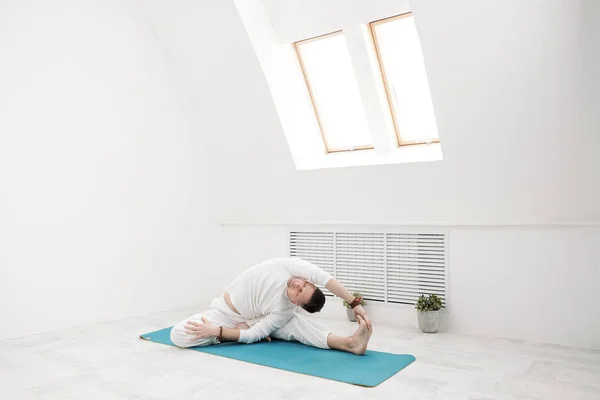 Um homem de roupas brancas faz exercícios. Yoga asanas e poses para alongamento e meditação . — Fotografia de Stock