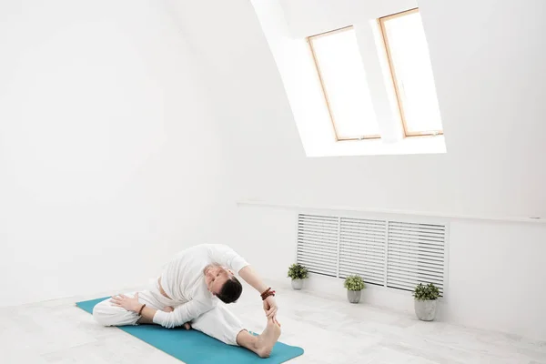 Um homem de roupas brancas faz exercícios. Yoga asanas e poses para alongamento e meditação . — Fotografia de Stock