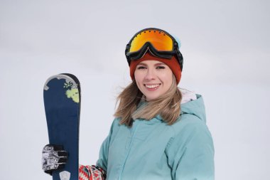 Takım elbise güzel bir genç çiğnemek bir aşırı spor, şapka ve kask kış yamacında bir maskeyle Alp kayaklar tutan.