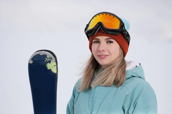 Uma bela mastigação jovem em um terno esportivo extremo, um chapéu e um capacete com uma máscara na encosta de inverno está segurando esquis alpinos . — Fotografia de Stock