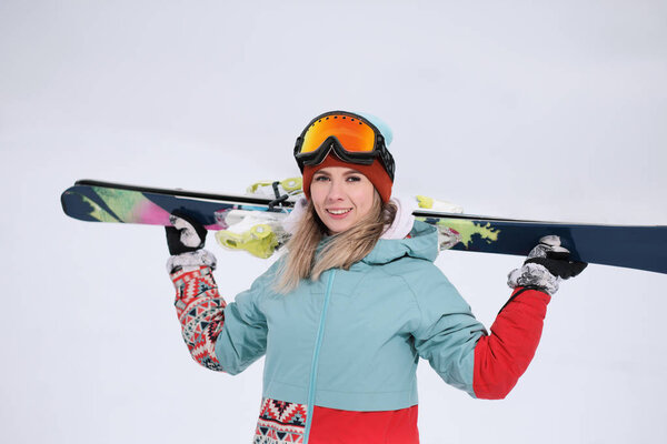 A beautiful young chew in an extreme sports suit, a hat and a helmet with a mask on the winter slope is holding alpine skis.