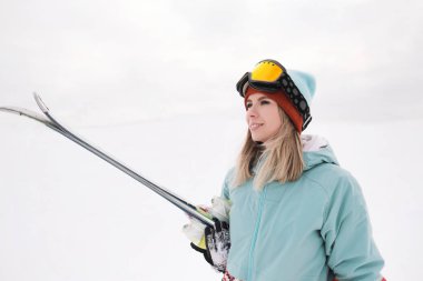 Takım elbise güzel bir genç çiğnemek bir aşırı spor, şapka ve kask kış yamacında bir maskeyle Alp kayaklar tutan.