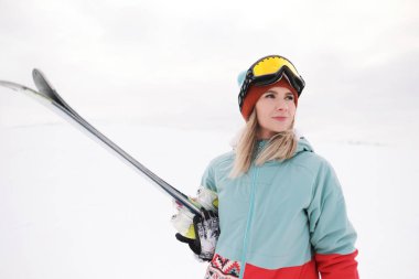 Takım elbise güzel bir genç çiğnemek bir aşırı spor, şapka ve kask kış yamacında bir maskeyle Alp kayaklar tutan.