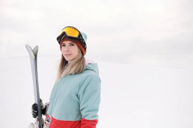 Takım elbise güzel bir genç çiğnemek bir aşırı spor, şapka ve kask kış yamacında bir maskeyle Alp kayaklar tutan.