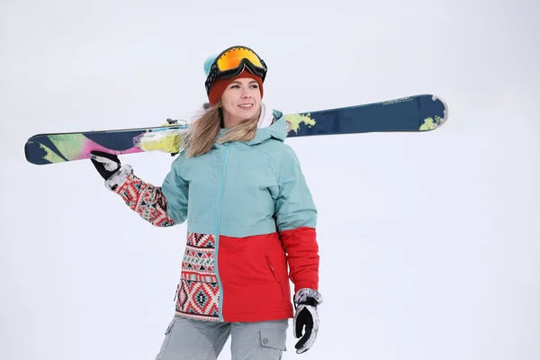 A beautiful young chew in an extreme sports suit, a hat and a helmet with a mask on the winter slope is holding alpine skis. — Stock Photo, Image