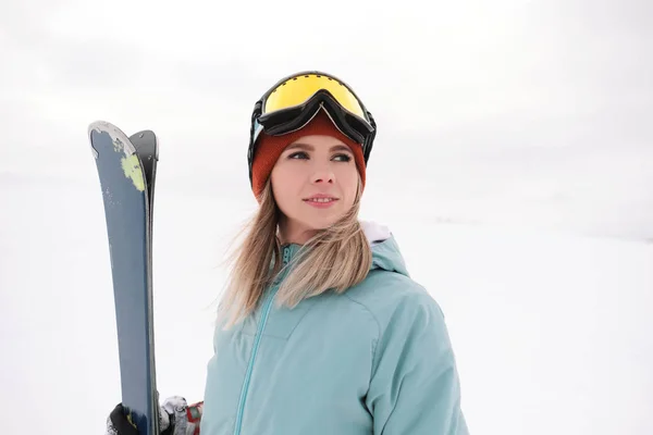 Uma bela mastigação jovem em um terno esportivo extremo, um chapéu e um capacete com uma máscara na encosta de inverno está segurando esquis alpinos . — Fotografia de Stock