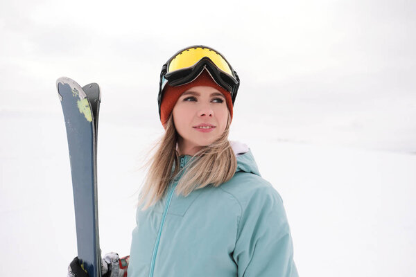 A beautiful young chew in an extreme sports suit, a hat and a helmet with a mask on the winter slope is holding alpine skis.