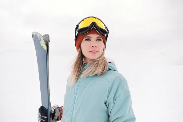 Uma bela mastigação jovem em um terno esportivo extremo, um chapéu e um capacete com uma máscara na encosta de inverno está segurando esquis alpinos . — Fotografia de Stock