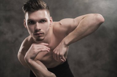 Genç bir erkek balet siyah tayt ve çıplak bir gövde ile dans hareketleri çerçevede bir gri grunge, duman ve ışıklar bir ışıkla gerçekleştirir.