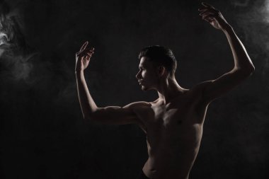 Genç bir erkek balet siyah tayt ve çıplak bir gövde ile dans hareketleri çerçevede bir gri grunge, duman ve ışıklar bir ışıkla gerçekleştirir.