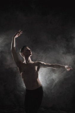 Genç bir erkek balet siyah tayt ve çıplak bir gövde ile dans hareketleri çerçevede bir gri grunge, duman ve ışıklar bir ışıkla gerçekleştirir.
