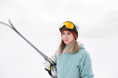 Spor aşırı bir güzel bir genç kız elbise, şapka ve kask kış yamacında bir maskeyle Alp kayaklar tutan.