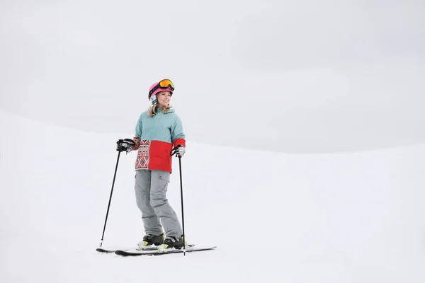 A beautiful young girl in an extreme sports suit, a hat and a helmet with a mask on the winter slope is holding alpine skis.