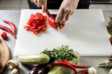 Erkek aşçı sebze salatası bir restoranda bir siyah önlük için keser. Beyaz kesme tahtası, closeup eller.