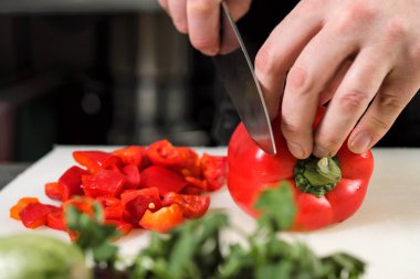 Erkek aşçı sebze salatası bir restoranda bir siyah önlük için keser. Beyaz kesme tahtası, closeup eller.