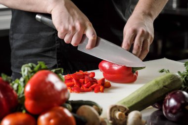 Erkek aşçı sebze salatası bir restoranda bir siyah önlük için keser. Beyaz kesme tahtası, closeup eller.