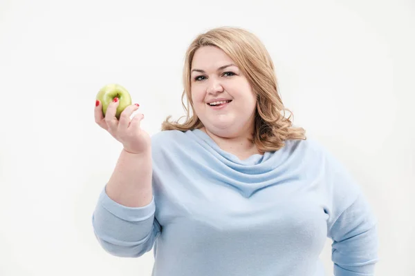 Jovem mulher gorda curvilínea em roupas azuis casuais em um fundo branco segurando uma maçã verde em sua mão. Dieta e nutrição adequada . — Fotografia de Stock