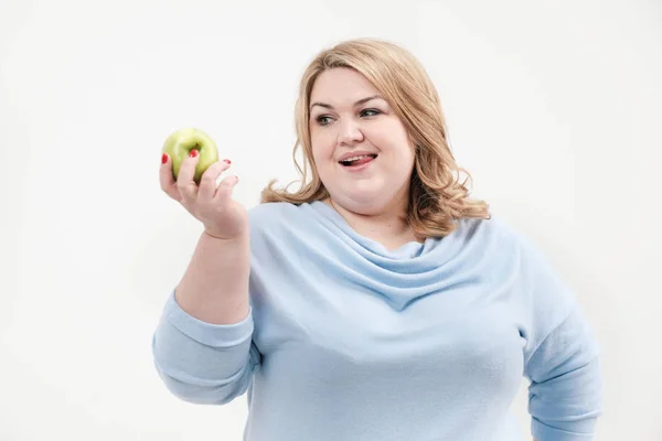 Jovem mulher gorda curvilínea em roupas azuis casuais em um fundo branco segurando uma maçã verde em sua mão. Dieta e nutrição adequada . — Fotografia de Stock