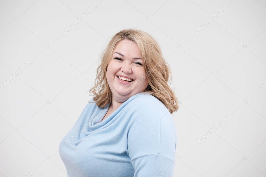 Young obese woman in casual blue clothes on a white background in the studio. Bodypositive.