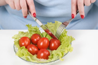 Genç yemyeşil şişman kadın rahat mavi masada beyaz bir arka plan üzerinde elbise ve domatesli sebze salata yiyor. Doğru beslenme ve diyet.