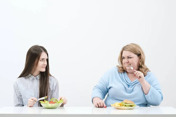 날씬한 여자 먹는 건강 식품, 뚱뚱한 여자 해로운 패스트 푸드를 먹는다. 흰색 배경, 식이 요법과 적절 한 영양 섭취의 테마. — 스톡 사진