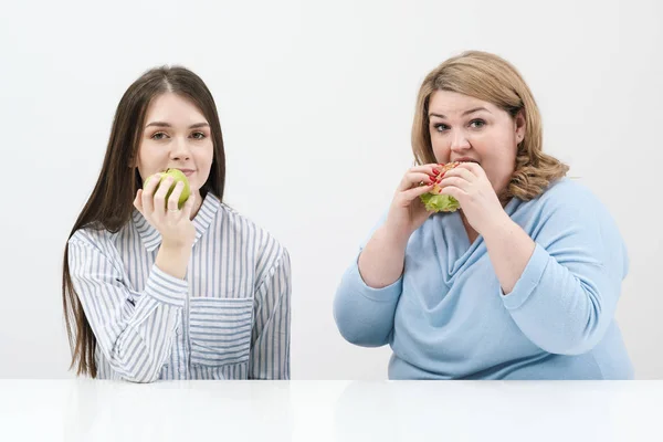 Струнка дівчина їсть здорову їжу, товста жінка їсть шкідливу фаст-фуду. На білому тлі тема дієти і правильного харчування . — стокове фото