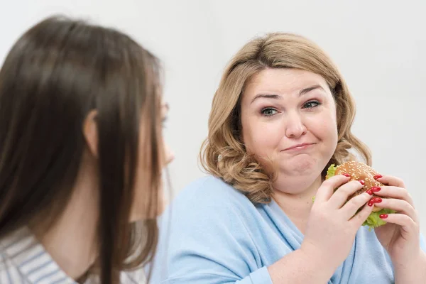 Chica delgada come comida saludable, mujer gorda come comida rápida dañina. Sobre un fondo blanco, el tema de la dieta y la nutrición adecuada . — Foto de Stock