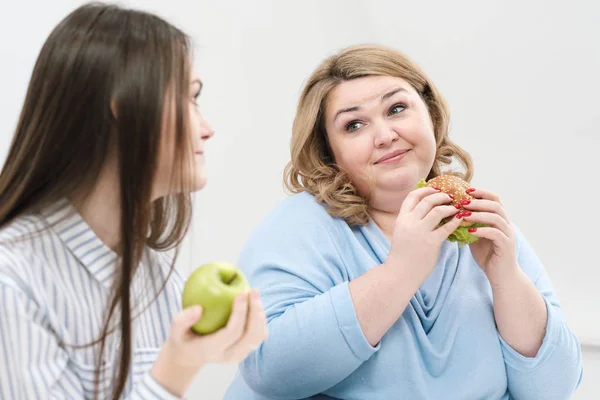 Slender girl eats healthy food, Fat woman eats harmful fast food. On a white background, the theme of diet and proper nutrition.