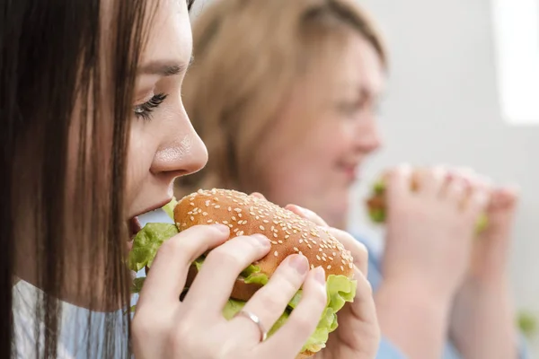 Deux filles, mince et grosse, blonde et brune, mangent des hamburgers. Sur un fond blanc, le thème de l'alimentation et une bonne nutrition . — Photo