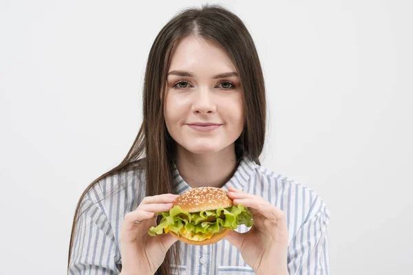 Mince fille brune tient dans ses mains un hamburger. Sur un fond blanc, le thème de l'alimentation et une bonne nutrition , — Photo