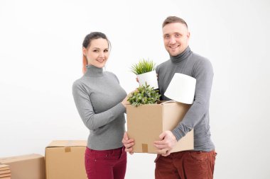 Genç bir aile, bir erkek ve bir kadın gri kazak yeni bir daire için hareket ediyor. Beyaz zemin üzerinde bir yük taşıyan kutular.