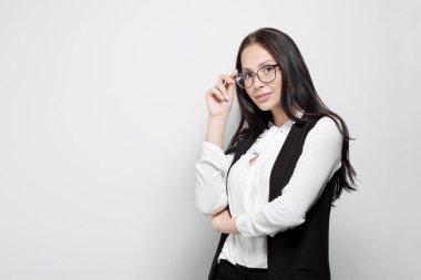 Beyaz bir duvarın arka planına karşı gözlük takan uzun kıvırcık saçlı güzel genç çekici esmer kız.