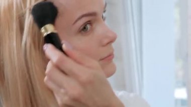 Ayna tarafından banyoda ayakta beyaz bornoz çekici orta yaşlı sarışın kadın. Makyaj uygular.