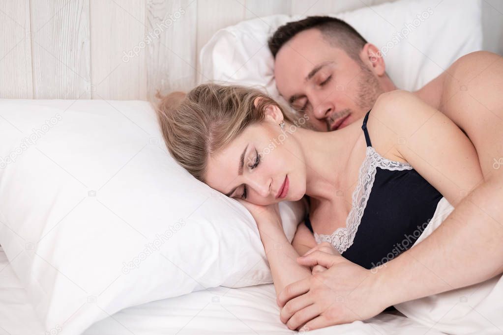 A married couple, a man and a woman, are lying in bed, hugging and sleeping.