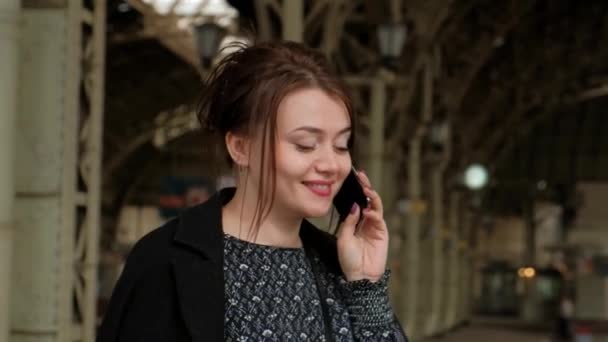Attractive middle-aged brunette woman uses a mobile phone at a train station. — Stock Video