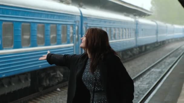 Mulher morena de meia-idade atraente em um casaco preto na estação ferroviária. Está a chover. Close-up de pernas andando em sapatos . — Vídeo de Stock