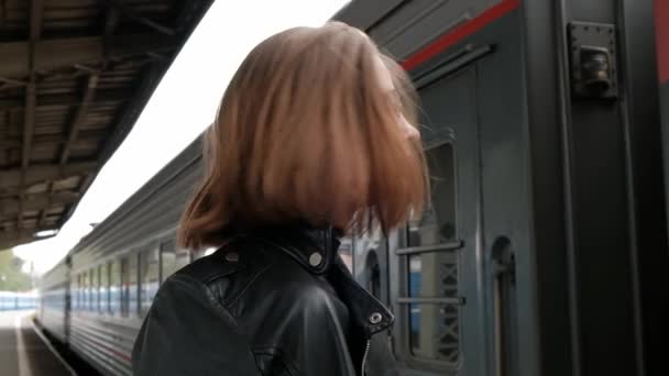 Jovem de cabelos vermelhos atraente com corte de cabelo curto, usando óculos e jaqueta de couro preto está de pé na bela estação ferroviária histórica de Vitebsk, em São Petersburgo . — Vídeo de Stock