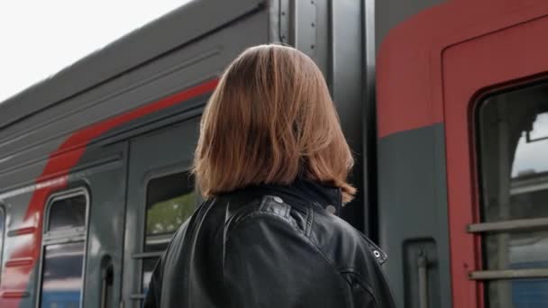 Jolie jeune femme aux cheveux roux avec une coupe courte, portant des lunettes et une veste en cuir noir est debout à la belle gare historique de Vitebsk à Saint-Pétersbourg . — Video